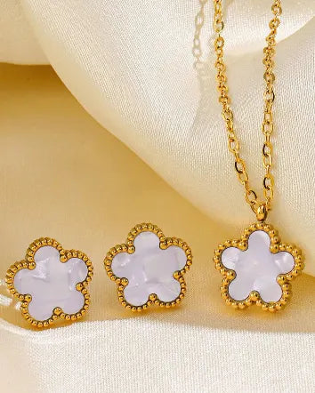 Gold necklace with white flower-shaped pendants on a beige fabric background