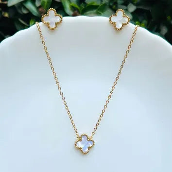 Gold necklace and earrings with clover-shaped pendants on a white stand.