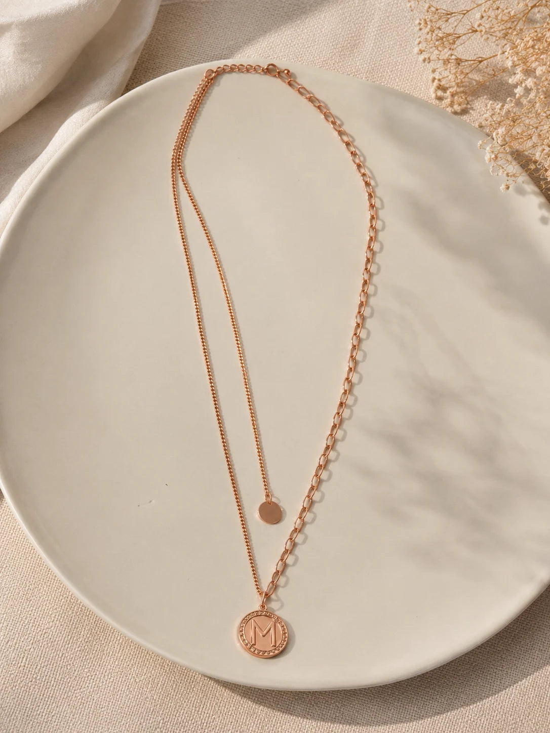 Rose gold necklace with circular pendants on a beige plate