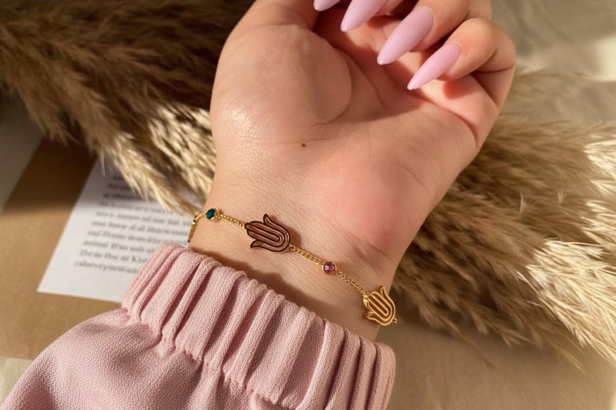 Hand wearing a gold bracelet with a hamsa design on a soft, textured background