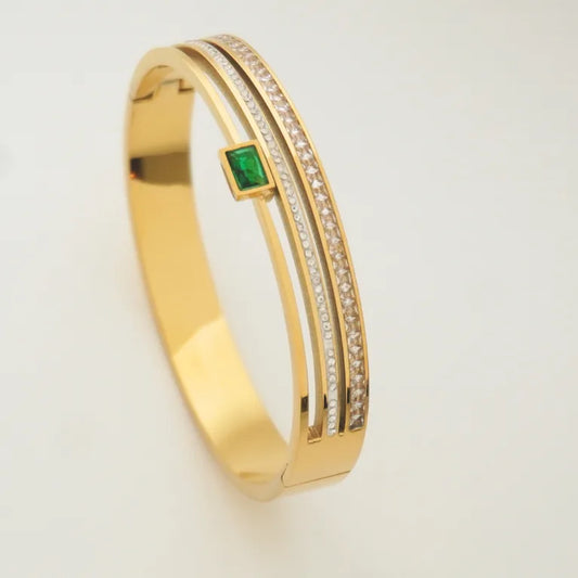Gold bracelet with a green gemstone on a light gray background