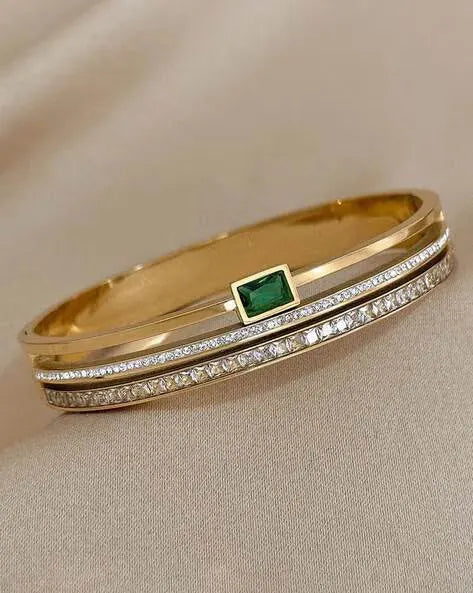 Gold bracelet with emerald and diamond accents on a beige background