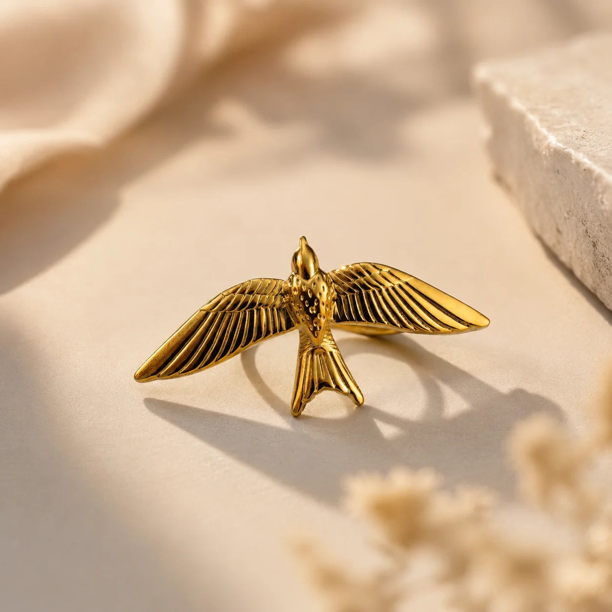 Gold bird wing ring with spread wings design on beige background, waterproof 316L stainless steel with 18K gold plating, anti tarnish statement ring

