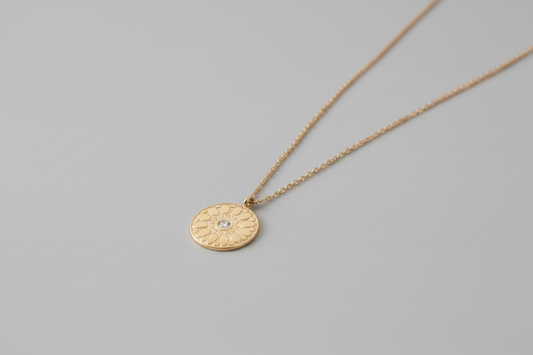 Gold necklace with a circular pendant on a stone surface